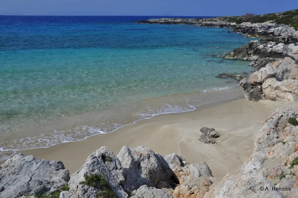 Coastal view of Macherida showing clear azure waters and a small secluded beach nestled against rugged cliffs.